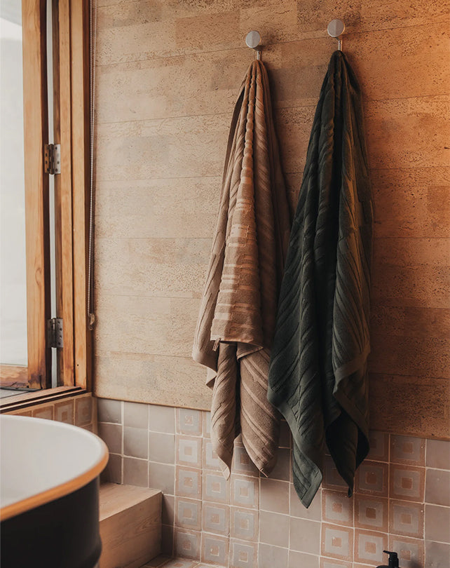 Two towels hanging on a towel rack against a tiled bathroom wall.
