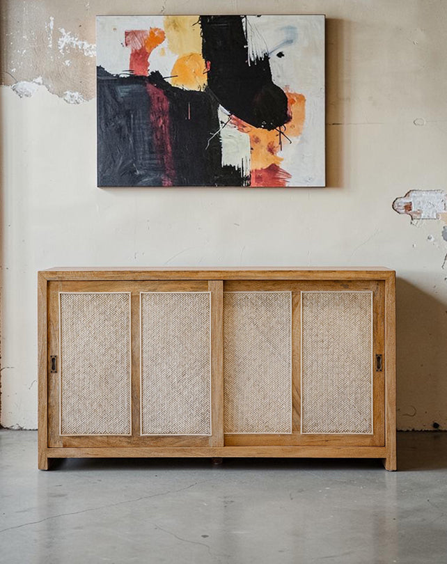 Wooden cabinet with woven doors below an abstract painting on a wall.