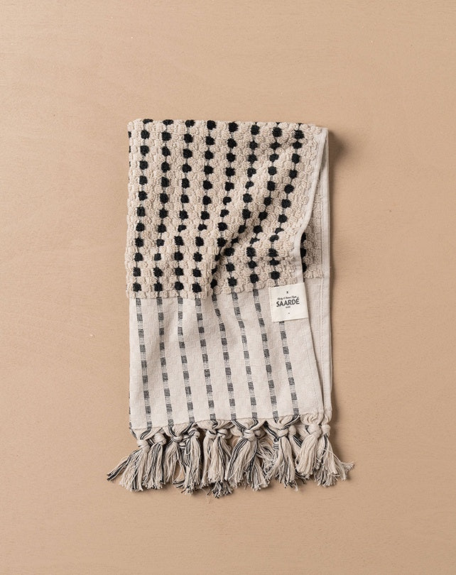 Textured towel with black dot pattern and tassels on a beige background