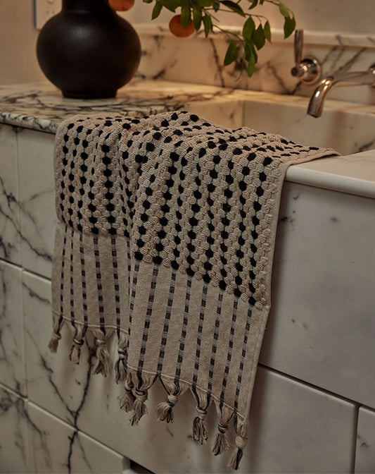 Textured towel with black dots and tassels draped over a marble countertop.