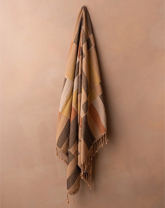 Plaid blanket with fringes hanging against a beige wall