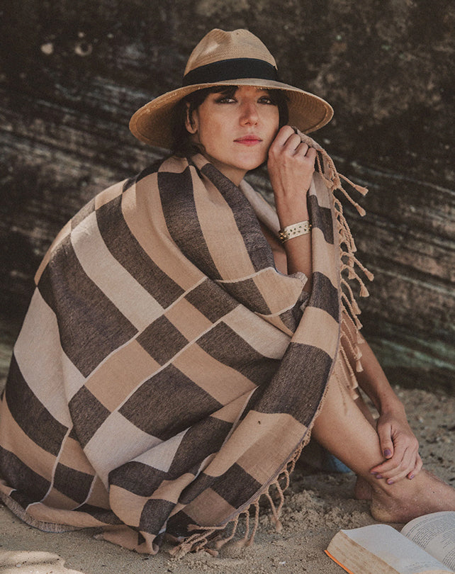 Woman sitting on a beach with a patterned blanket and hat