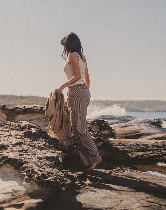 Person standing on a rocky beach holding a bag, with a scenic view of water and sky.