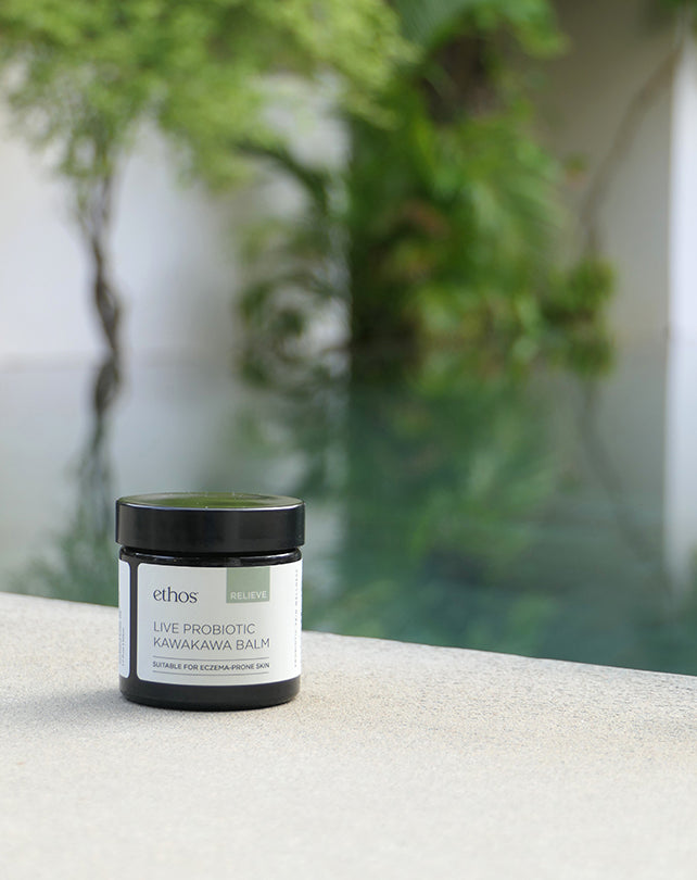 Jar of 'ethos' balm on a stone surface with greenery in the background