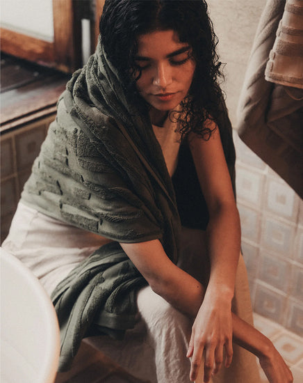Woman wrapped in a green towel sitting on a bed in a bedroom setting
