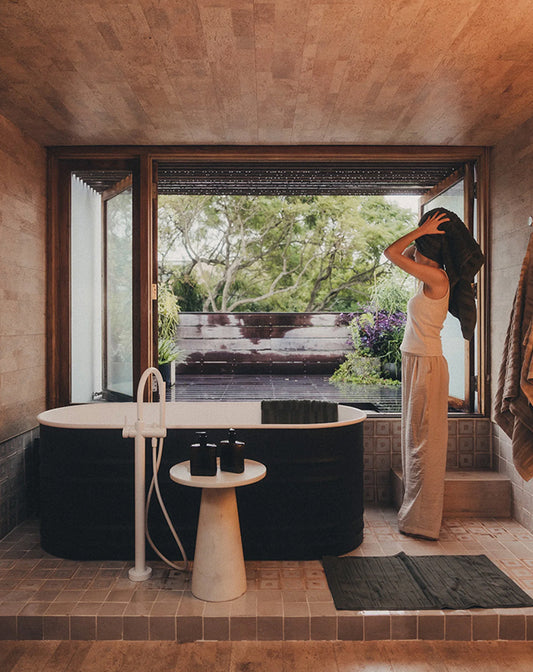 Person standing by a modern outdoor bathtub with a view of trees and a garden.