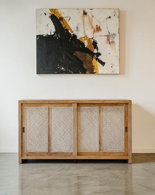 Wooden cabinet with textured doors below an abstract painting on a white wall.