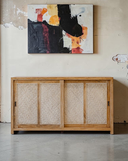 Wooden cabinet with woven doors below an abstract painting on a wall.