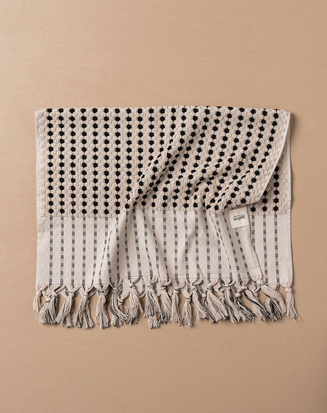 Textured blanket with black pattern and tassels on a beige background