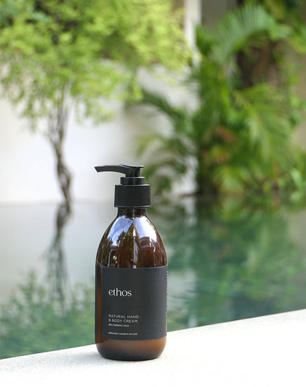 Brown bottle with black pump labeled 'ethos' on a reflective surface with greenery in the background