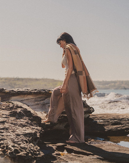 Woman standing on a rocky beach with a scarf draped over her shoulders