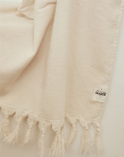 Beige woven fabric with tassels and a visible brand label on a light background