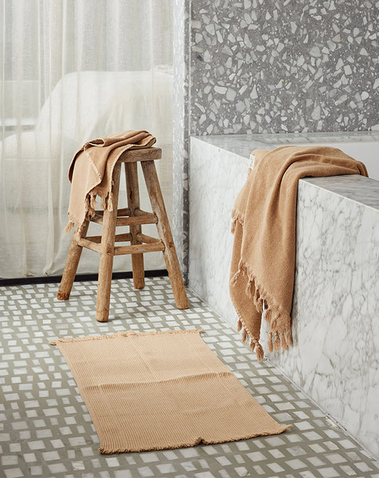 Bathroom with wooden stool, bath mat, and towel draped over a bathtub.