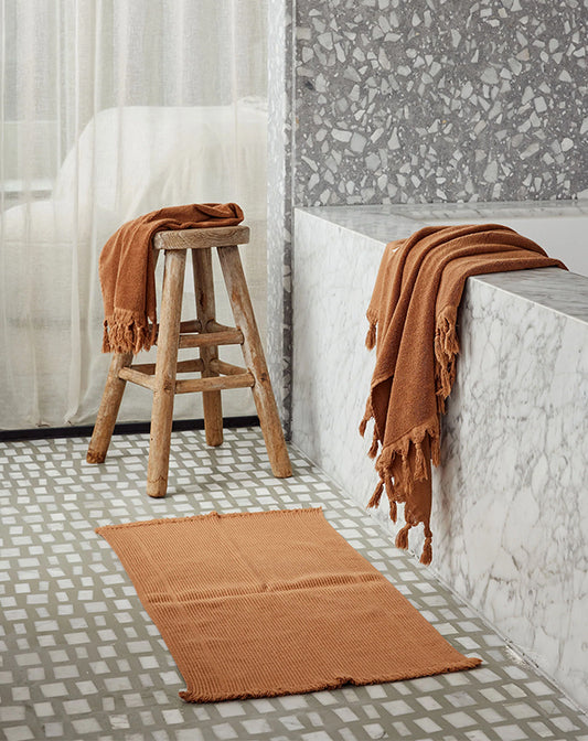 Bathroom with terrazzo tiles, a stool, and a rug with a brown towel draped over it.